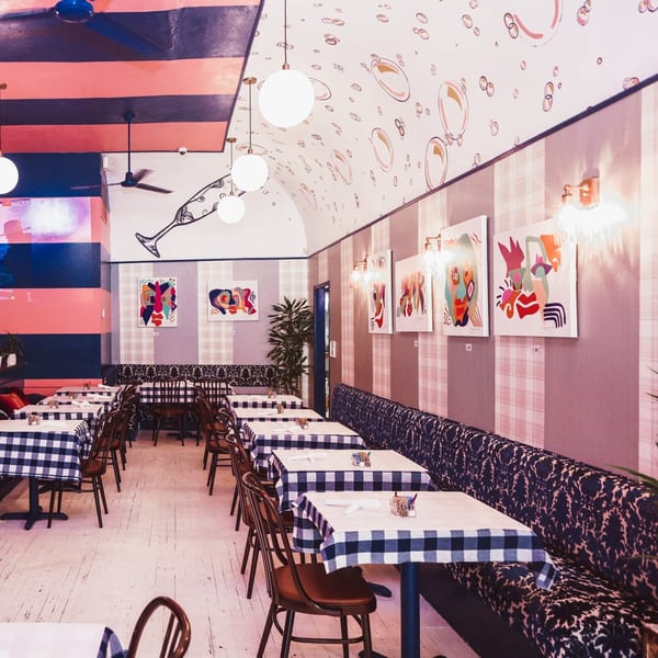 The Breakfast Boys dining room with checkered tablecloths, abstract art, and a pink and blue striped ceiling.