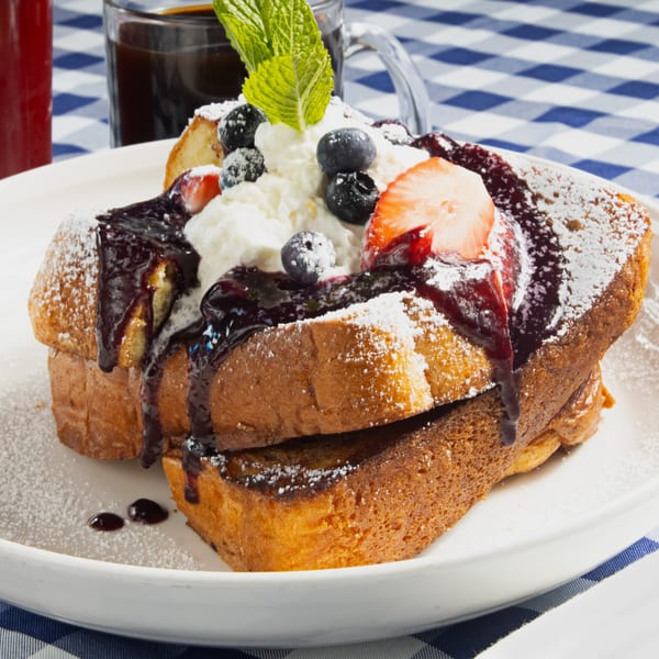 Thick-cut French toast with berry compote, whipped cream, fresh berries, and powdered sugar.
