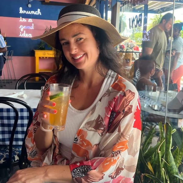 A smiling woman in a hat holds a drink at The Breakfast Boys, with a "brunch is a good idea" neon sign.