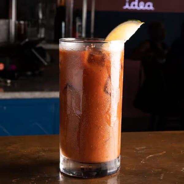A tall glass of Bloody Mary with a lemon wedge, condensation on the glass, on a wooden table.