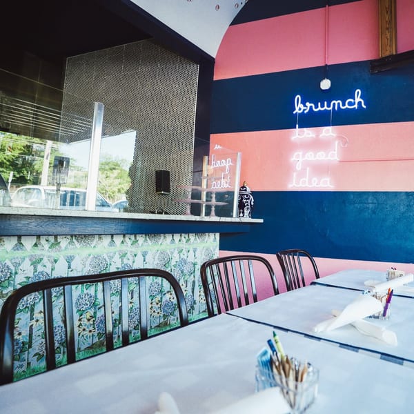 The Breakfast Boys restaurant interior with a neon "brunch is a good idea" sign and set tables.