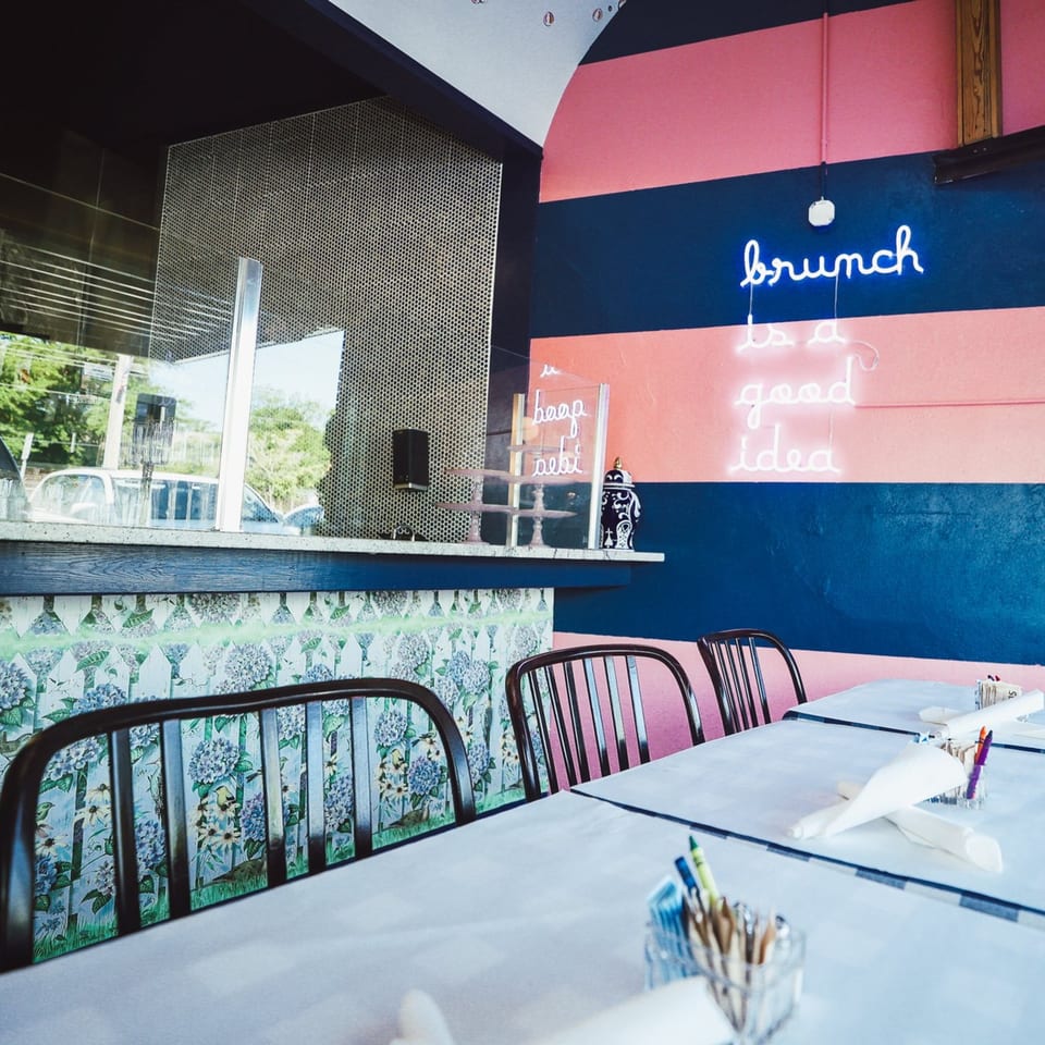 The Breakfast Boys restaurant interior with a neon "brunch is a good idea" sign and set tables.