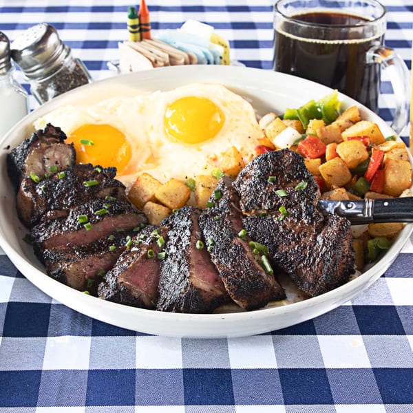The Breakfast Boys' steak and eggs brunch with home fries on a blue and white checkered tablecloth.