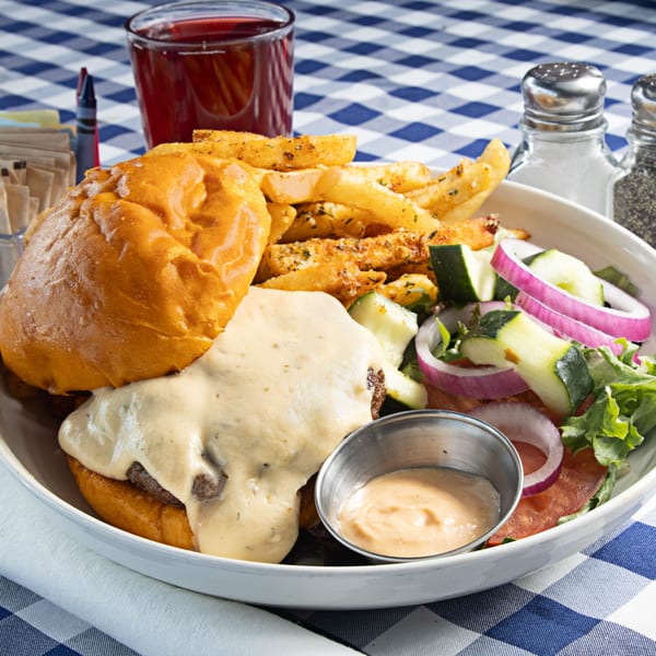 The Breakfast Boys' cheeseburger with fries, side salad, and a drink on a blue and white checkered tablecloth.