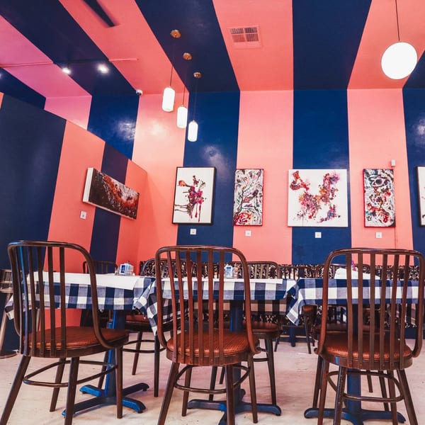 The Breakfast Boys dining room with bold pink and blue striped walls, abstract art, and checkered tablecloths.