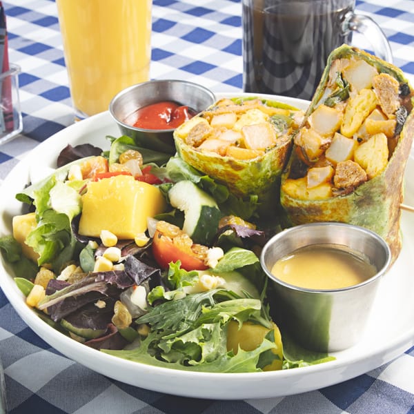 A breakfast burrito with potatoes and eggs, served with a side salad and dressing on a checkered tablecloth.