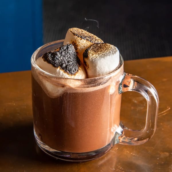 Steaming hot chocolate in a clear mug, topped with three perfectly toasted marshmallows.
