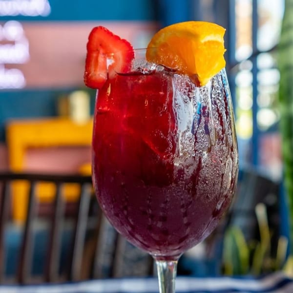A chilled glass of red sangria, garnished with a strawberry slice and orange wedge, at The Breakfast Boys.