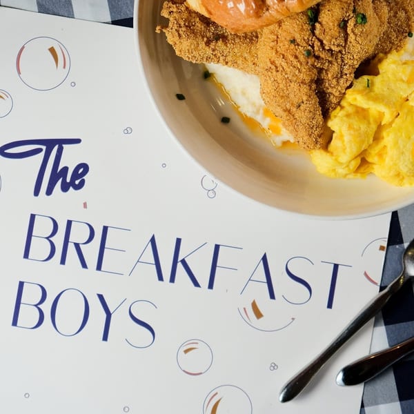 A plate of fried chicken, grits, and scrambled eggs next to a "The Breakfast Boys" menu.