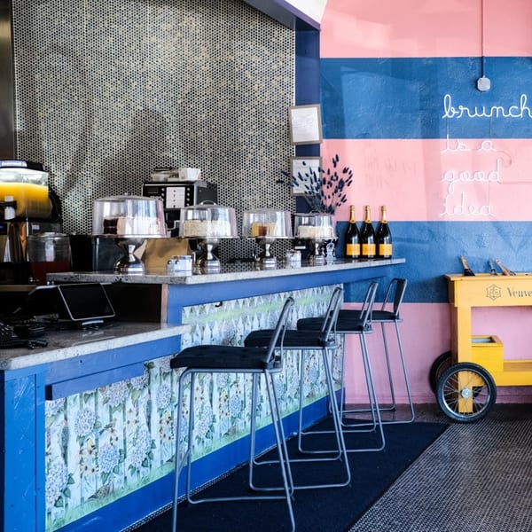 The Breakfast Boys' colorful brunch bar with cakes, juice, champagne, and a neon sign.